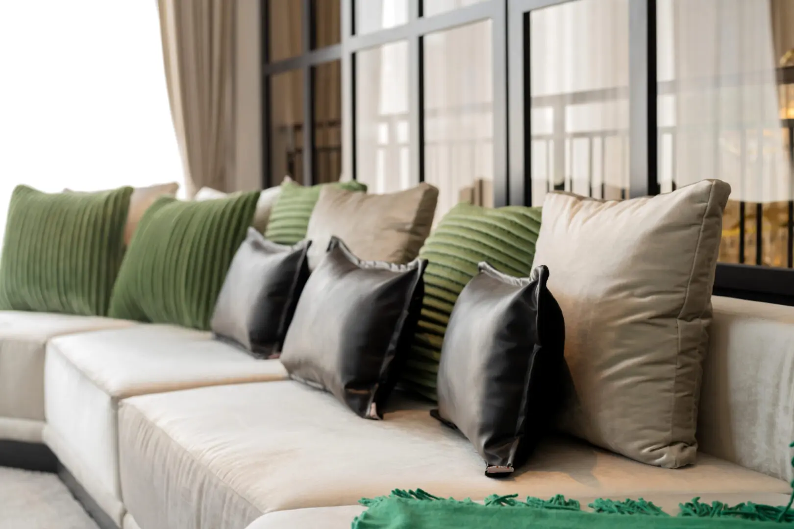 A row of pillows on a couch in front of windows.
