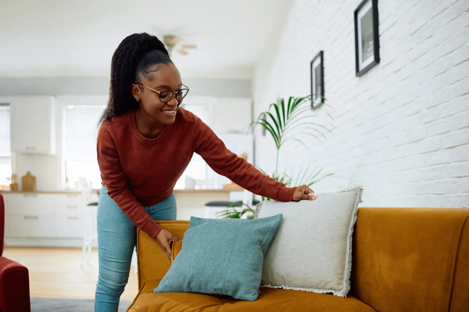 Woman arranging cushions on a yellow sofa.